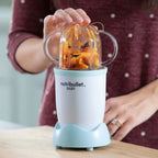 Mujer presionando el vaso corto con asas de la Nutribullet Baby de 200W para triturar pasta con salsa roja - Ferretería La Palma - 1690012