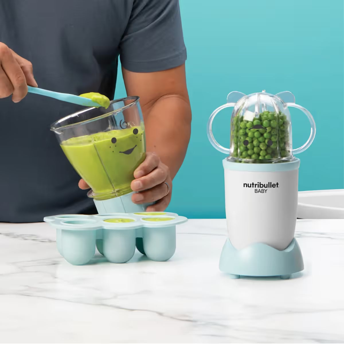 Persona sirviendo puré verde con espátula en la bandeja de congelación junto al extractor Nutribullet Baby lleno de guisantes - Ferretería La Palma - 1690012