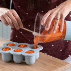 Mujer vertiendo puré de frutas con espátula desde el vaso grande de la Nutribullet Baby de 200W hacia la bandeja de congelación - Ferretería La Palma - 1690012