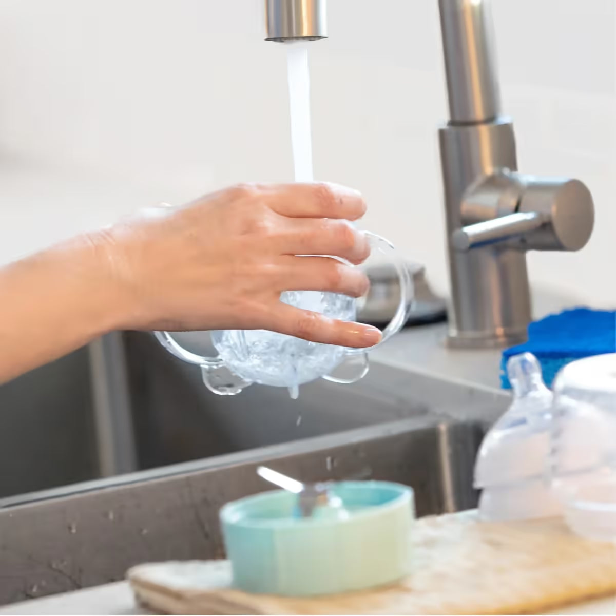 Mano lavando bajo el grifo el vaso con asas del extractor infantil Nutribullet Baby de 200W en un fregadero - Ferretería La Palma - 1690012