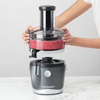 Manos sosteniendo y separando el contenedor de pulpa con residuos rojos de la base del extractor Nutribullet Juicer 800W - Ferretería La Palma - 1690019