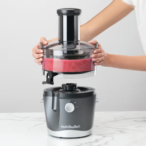 Manos sosteniendo y separando el contenedor de pulpa con residuos rojos de la base del extractor Nutribullet Juicer 800W - Ferretería La Palma - 1690019