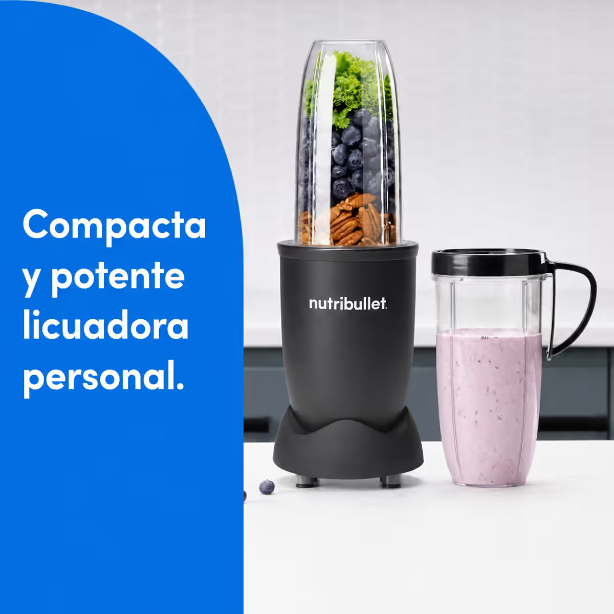 Vista frontal de la licuadora personal Nutribullet Pro de 900W con arándanos, nueces y vegetales en el vaso principal, junto a un licuado morado en el vaso con anillo con asa, sobre un diseño de fondo azul con texto informativo - Almacén La Palma - 1690115