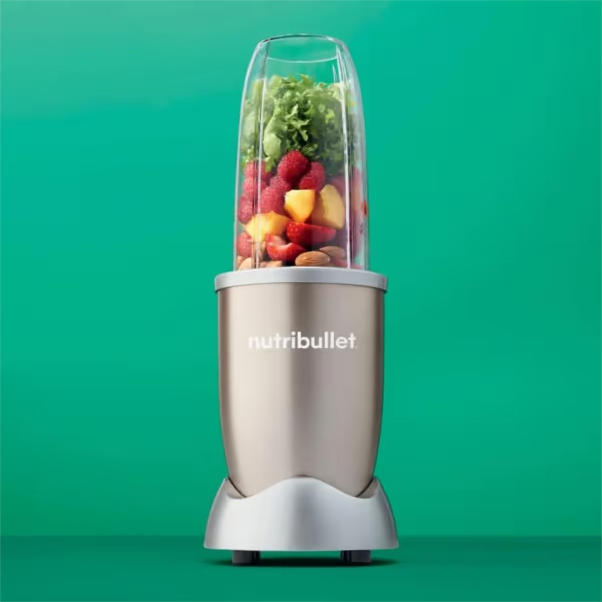 Licuadora personal Nutribullet Pro 900W en color champagne con un vaso lleno de fresas, piña, almendras y espinacas sobre un fondo verde - Ferretería La Palma - 1690013