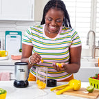 Mujer sonriendo en una cocina mientras coloca trozos de mango en un vaso de la licuadora personal Magic Bullet Original - Almacén La Palma - 1690001