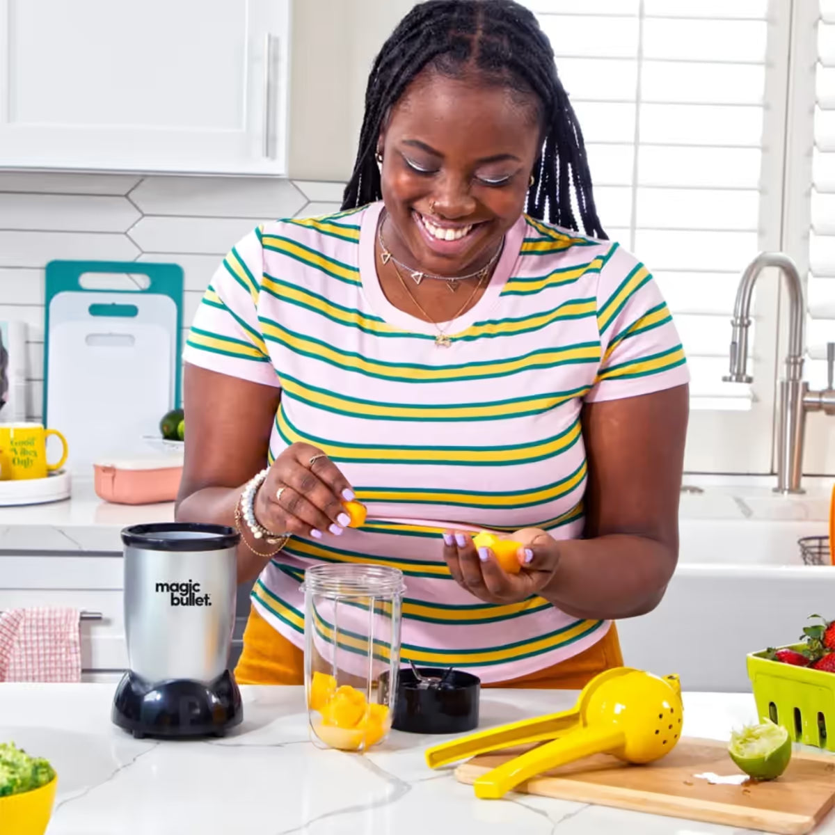 Mujer sonriendo en una cocina mientras coloca trozos de mango en un vaso de la licuadora personal Magic Bullet Original - Almacén La Palma - 1690001