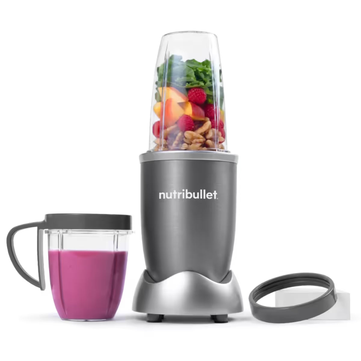 Vista frontal de la licuadora personal Nutribullet Original de 600W con frutas, nueces y vegetales en el vaso principal, un licuado de frutos del bosque en el vaso con anillo con asa y un anillo de comodidad - Almacén La Palma - 1690000