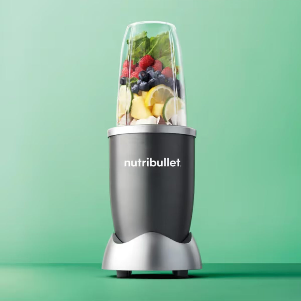 Vista frontal de la licuadora personal Nutribullet Original de 600W con frutas y vegetales en el vaso principal sobre un fondo verde - Almacén La Palma - 1690000