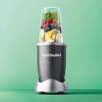 Vista frontal de la licuadora personal Nutribullet Original de 600W con frutas y vegetales en el vaso principal sobre un fondo verde - Almacén La Palma - 1690000