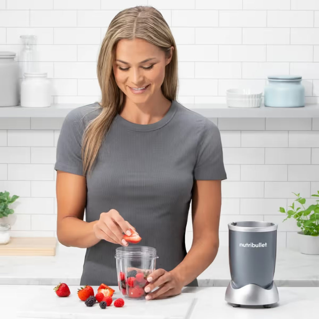 Mujer sonriendo en una cocina mientras coloca fresas en un vaso de la licuadora personal Nutribullet Original de 600W - Almacén La Palma - 1690000