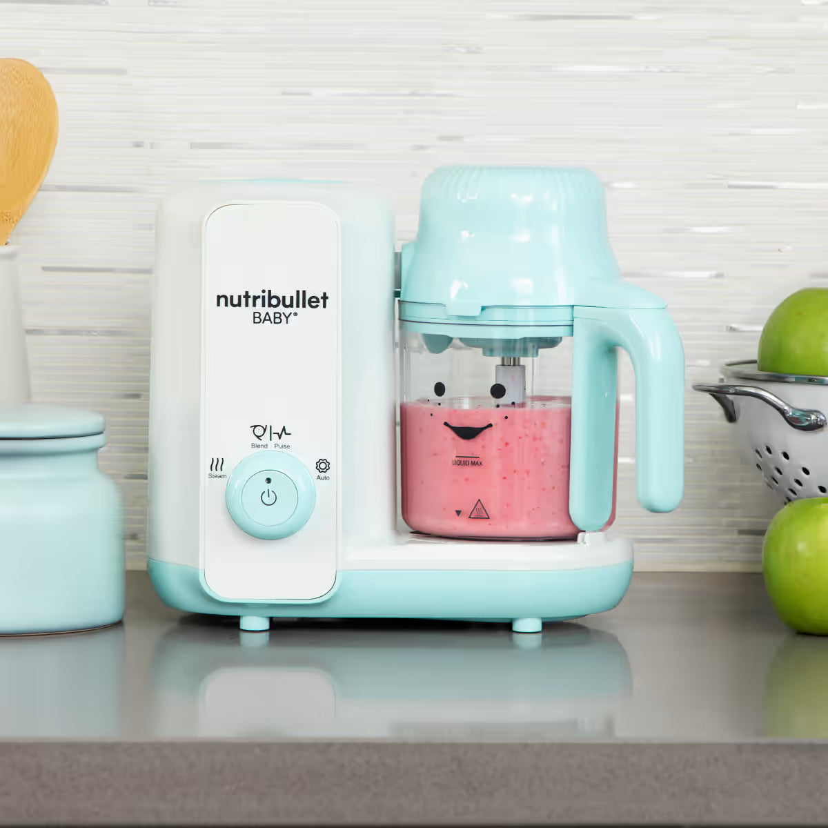 Procesador Nutribullet Baby Steam y Blend preparando un puré rosa en el vaso, sobre una encimera de cocina con manzanas verdes al lado - Ferretería La Palma - 1690018