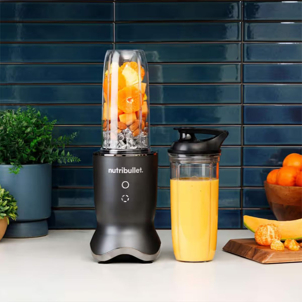 Extractor de nutrientes Nutribullet Ultra 1200W en una cocina junto a su vaso con tapadera de viaje con smoothie de naranja y frutas frescas - Ferretería La Palma - 1690110