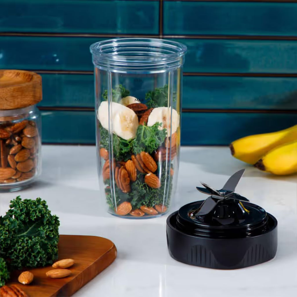 Vaso de licuadora Nutribullet Ultra 1200W con rodajas de banano, kale y almendras junto a la base de cuchillas sobre la encimera - Ferretería La Palma - 1690110