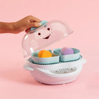 Mano levantando la tapa transparente de la vaporera Nutribullet Turbo Baby 900W para mostrar dos recipientes con alimentos sobre un fondo rosa - Ferretería La Palma - 1690014