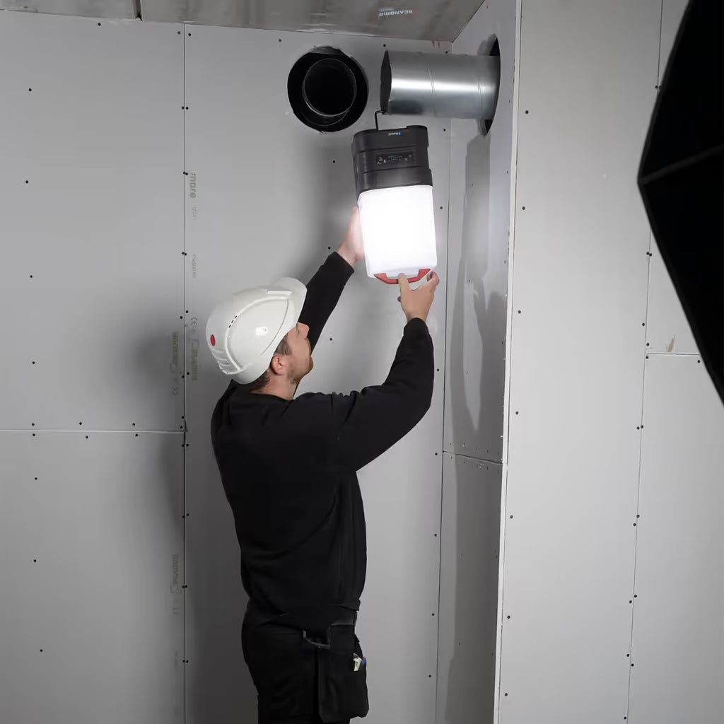 Operario con casco de seguridad colgando el reflector industrial LED Scangrip AREA 10 CONNECT de un ducto metálico para iluminar una obra - Ferretería La Palma - 1870011