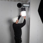 Operario con casco de seguridad colgando el reflector industrial LED Scangrip AREA 10 CONNECT de un ducto metálico para iluminar una obra - Ferretería La Palma - 1870011
