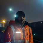 Trabajador con chaqueta de seguridad de alta visibilidad naranja utilizando la lámpara portátil Scangrip FLEX WEAR sujeta al pecho por la noche - Ferretería La Palma - 1870002