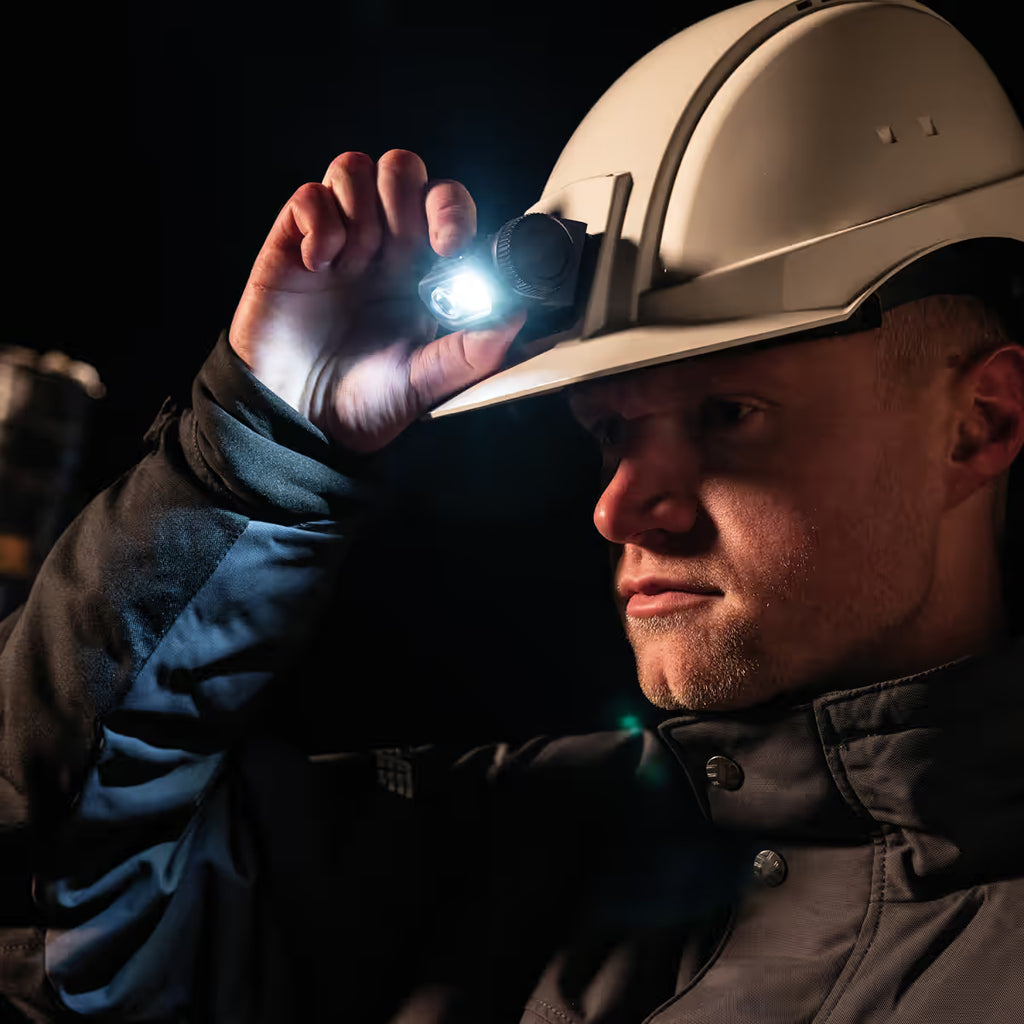 Trabajador utilizando la lámpara LED Scangrip HORIZON encendida sobre su casco de seguridad blanco en un entorno oscuro - Ferretería La Palma - 1870003
