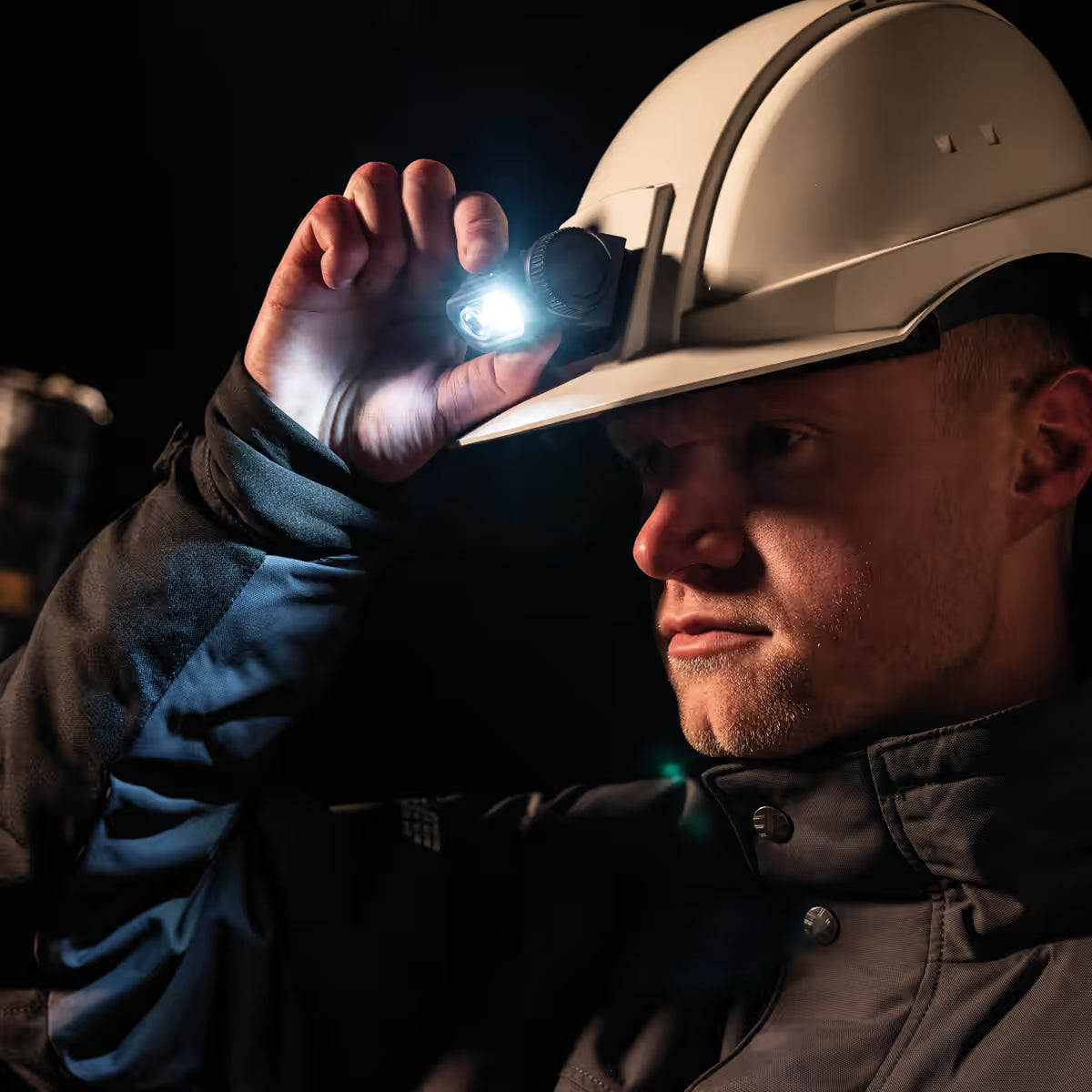Trabajador utilizando la lámpara LED Scangrip HORIZON encendida sobre su casco de seguridad blanco en un entorno oscuro - Ferretería La Palma - 1870003
