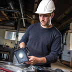 Operario con casco de seguridad utilizando el reflector LED compacto industrial Scangrip NOVA 2 CONNECT encendido para iluminar su mesa de trabajo en un taller - Ferretería La Palma - 1870008