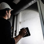 Operario con casco de seguridad utilizando el reflector LED compacto industrial Scangrip NOVA 2 CONNECT para iluminar una pared y tuberías en un espacio de trabajo oscuro - Ferretería La Palma - 1870008