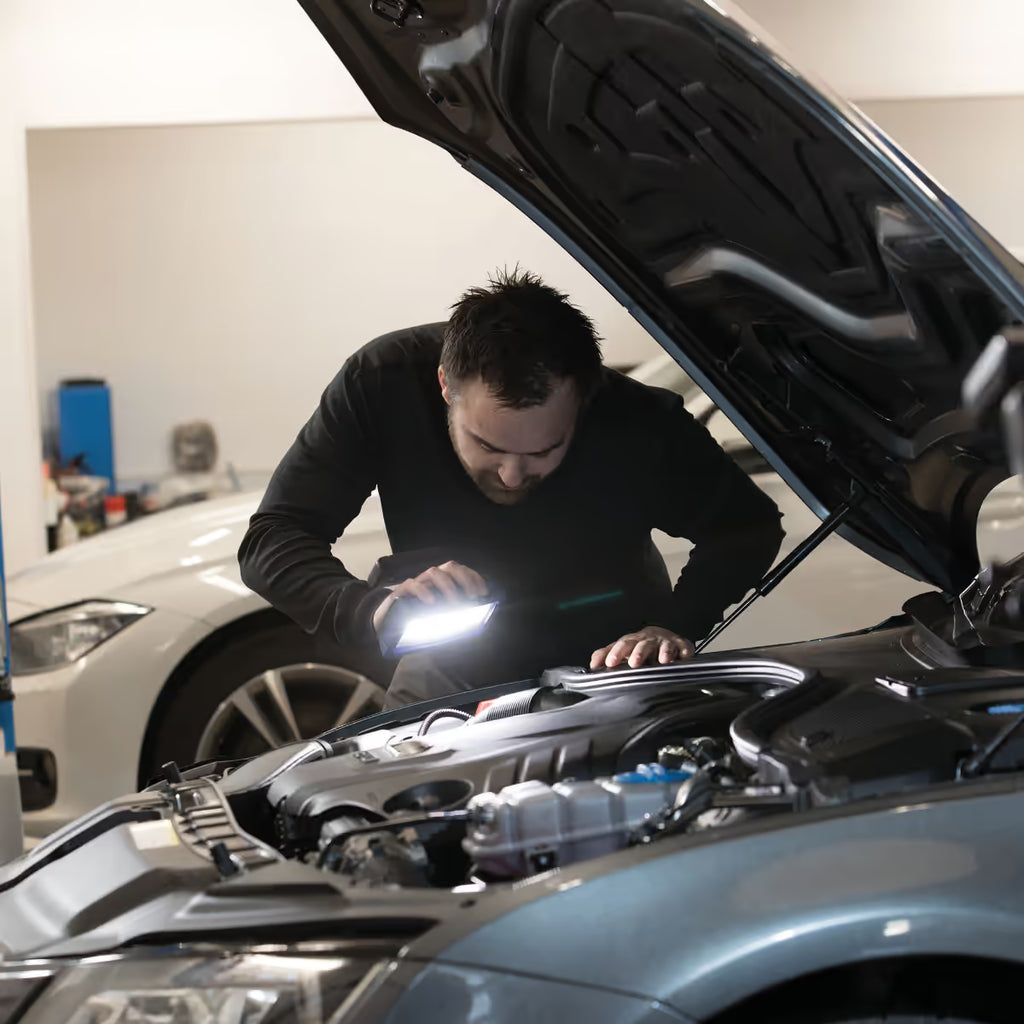 Mecánico inspeccionando el motor de un automóvil en un taller utilizando el reflector industrial LED Scangrip STAR encendido - Ferretería La Palma - 1870001