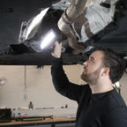 Mecánico inspeccionando la parte inferior de un automóvil en un taller utilizando el reflector industrial LED Scangrip STAR encendido - Ferretería La Palma - 1870001
