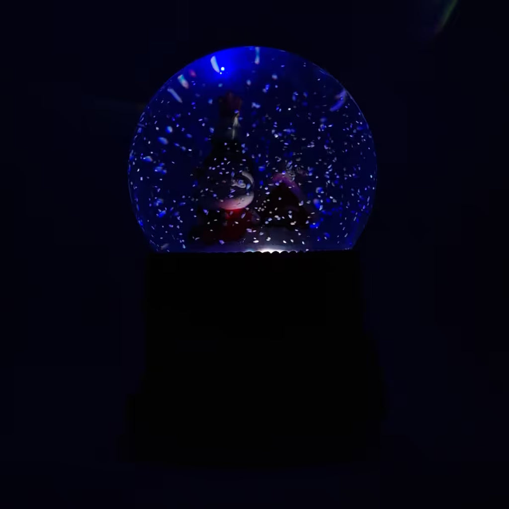 Vista frontal de la bola de nieve musical navideña Starlights Santa Claus mostrando luz en color azul en un fondo oscuro - Ferretería La Palma - 1800000