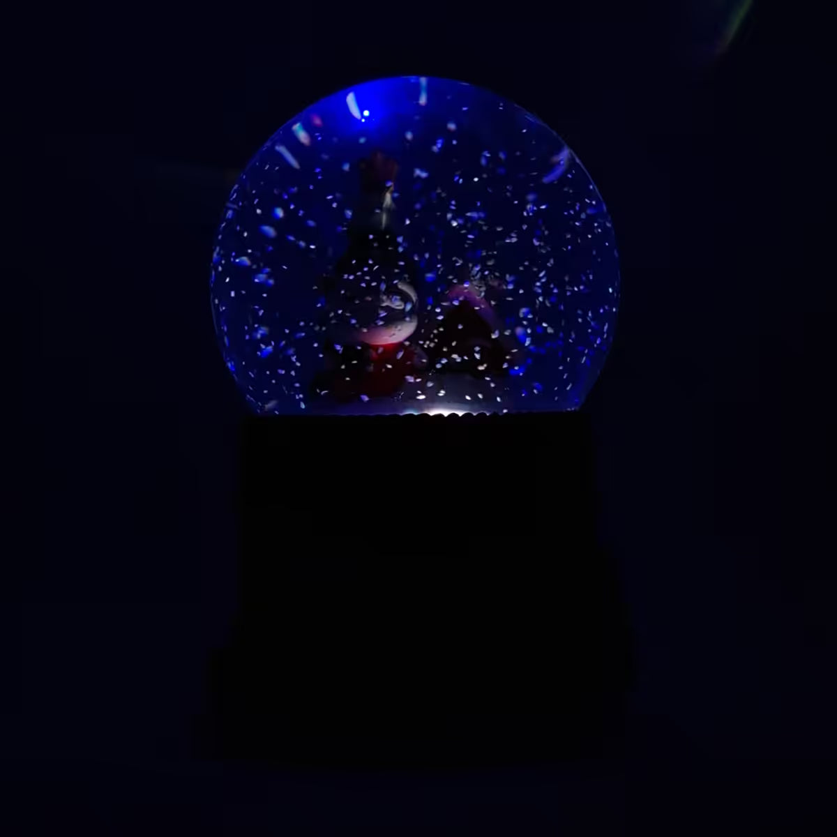 Vista frontal de la bola de nieve musical navideña Starlights Santa Claus mostrando luz en color azul en un fondo oscuro - Ferretería La Palma - 1800000