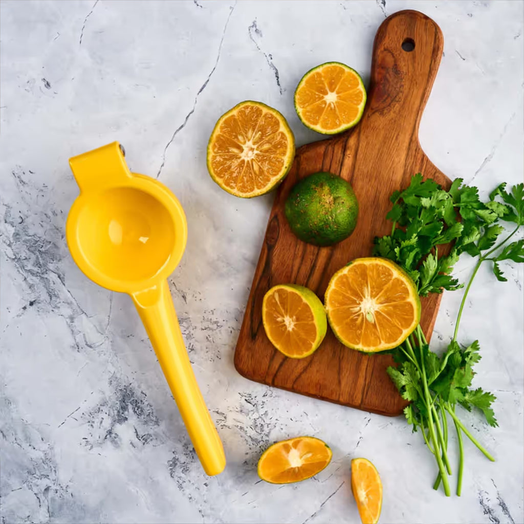 Exprimidor de limones manual Victoria de aluminio fundido color amarillo en una ambientación de cocina, junto a una tabla de madera con limones cortados y cilantro sobre una superficie de mármol - Ferretería La Palma - 1050001
