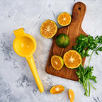 Exprimidor de limones manual Victoria de aluminio fundido color amarillo en una ambientación de cocina, junto a una tabla de madera con limones cortados y cilantro sobre una superficie de mármol - Ferretería La Palma - 1050001