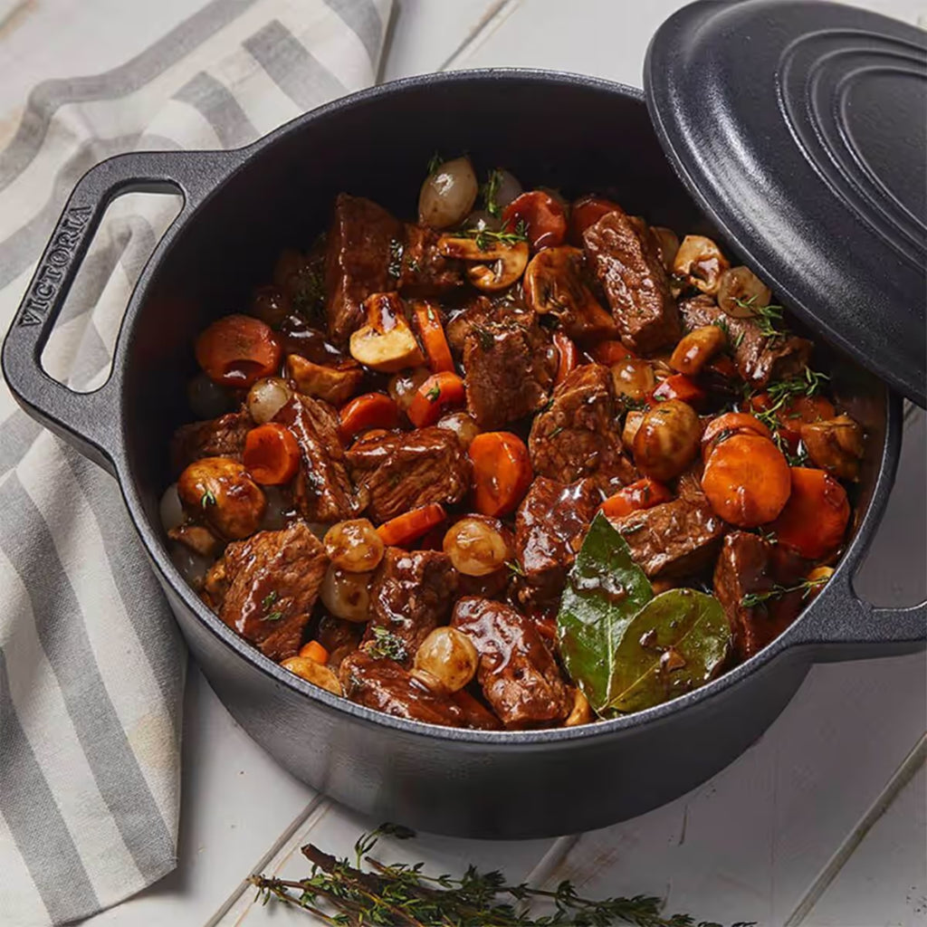 Vista superior en perspectiva del horno holandés Victoria de 5.7 litros en hierro fundido esmaltado con un estofado de carne, champiñones, zanahorias y cebollitas sobre una mesa de madera blanca - Ferretería La Palma - 1050083