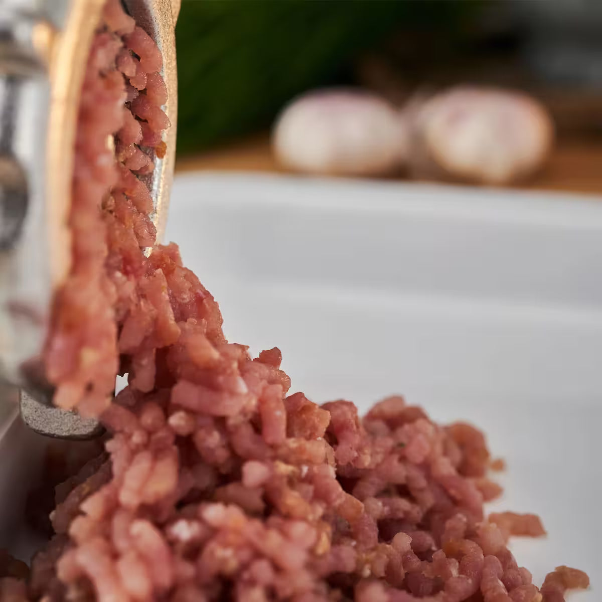 Primer plano de carne recién molida saliendo de un molino manual Victoria número 10 de hierro fundido, destacando la textura de la molienda para hamburguesas o embutidos - Ferretería La Palma - 1440002