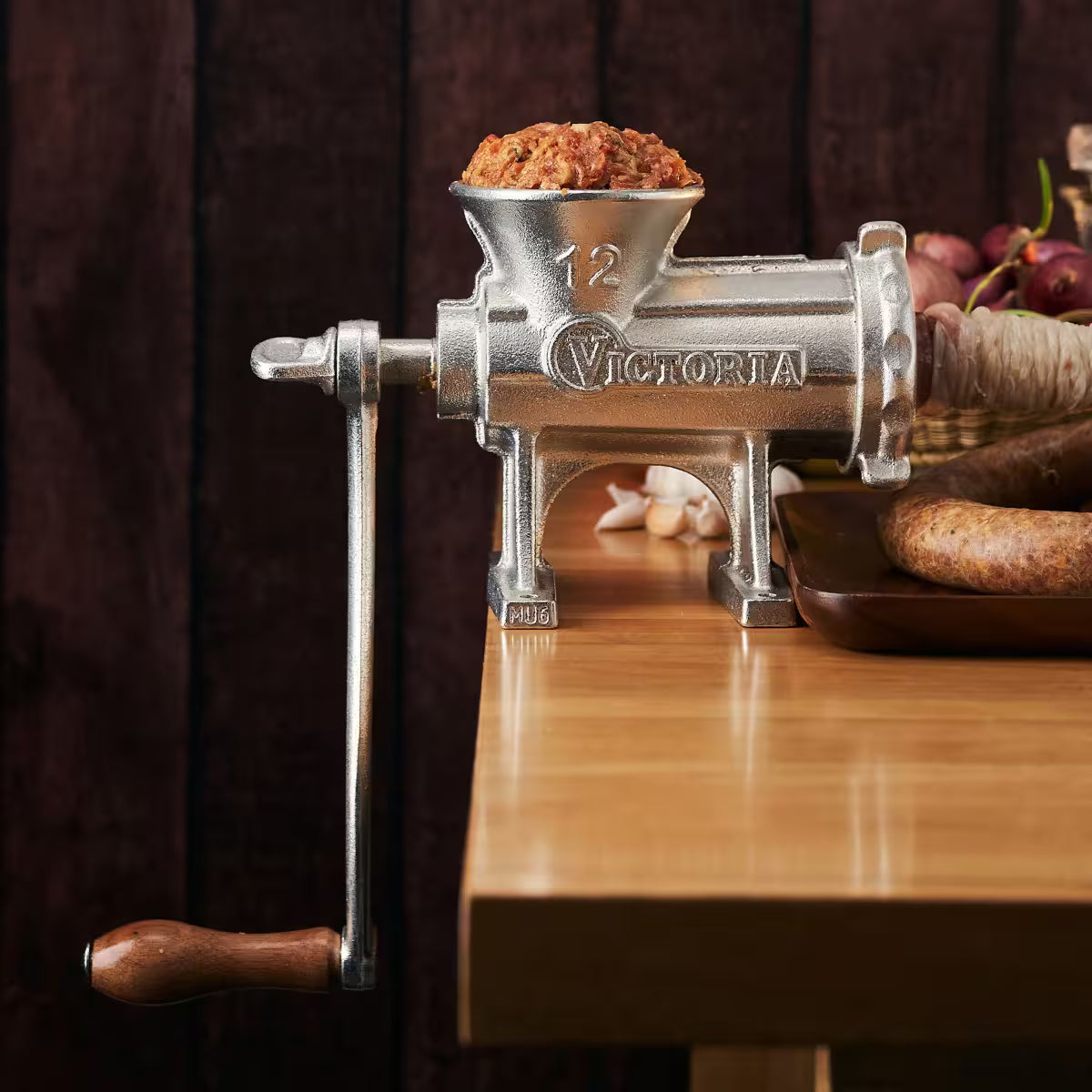 Molino de carne manual Victoria número 12 de hierro fundido estañado para uso pesado, instalado sobre mesa de madera y en proceso de embutido de chorizos artesanales - Ferretería La Palma - 1440003