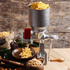 Molino de granos manual Victoria con tolva alta de 1.5 litros en uso, moliendo granos de maíz amarillo en una cocina rústica, junto a sacos de café y recipientes con maní, diseñado en hierro fundido estañado para alta durabilidad - Ferretería La Palma - 1040006
