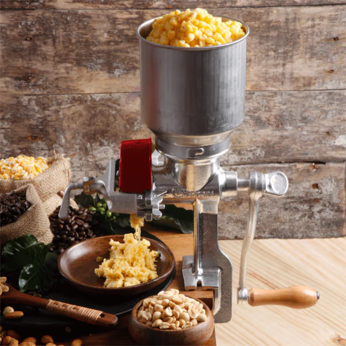 Molino de granos manual Victoria con tolva alta de 1.5 litros en uso, moliendo granos de maíz amarillo en una cocina rústica, junto a sacos de café y recipientes con maní, diseñado en hierro fundido estañado para alta durabilidad - Ferretería La Palma - 1040006