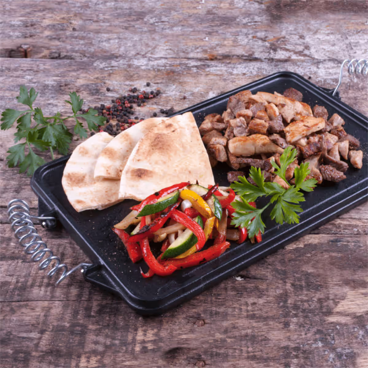 Vista en perspectiva de la cara lisa de la plancha reversible Victoria de 33x21 cm en hierro fundido curado con carne picada, pan pita y vegetales salteados servidos sobre una mesa de madera - Ferretería La Palma - 1050021