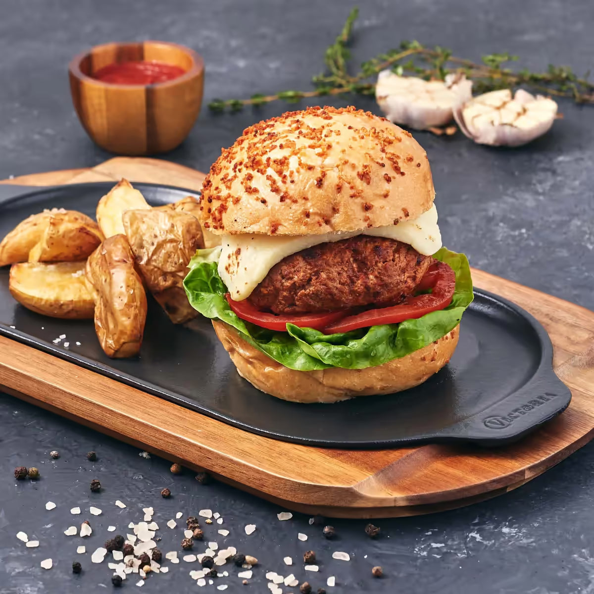 Vista en perspectiva de la plancha ovalada Victoria de 34x17 cm en hierro fundido esmaltado con una hamburguesa y papas servidas sobre una base de madera - Ferretería La Palma - 1050040