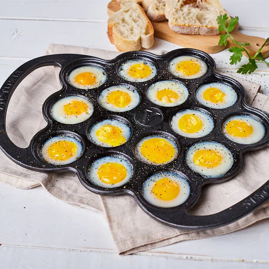 Vista superior en perspectiva de la provoletera Victoria en hierro fundido esmaltado con huevos de codorniz preparados y sazonados, acompañada de pan sobre una superficie clara - Ferretería La Palma - 1050076