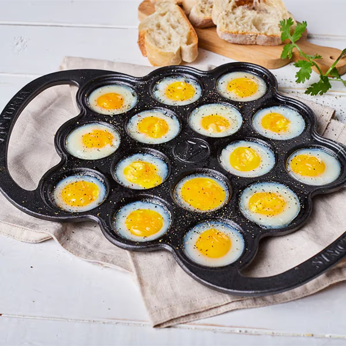 Vista superior en perspectiva de la provoletera Victoria en hierro fundido esmaltado con huevos de codorniz preparados y sazonados, acompañada de pan sobre una superficie clara - Ferretería La Palma - 1050076