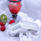 Vista en perspectiva del raspador de hielo manual Victoria en hierro fundido estañado ambientado con hielo raspado, una granizada y frutas frescas - Ferretería La Palma - 1050031