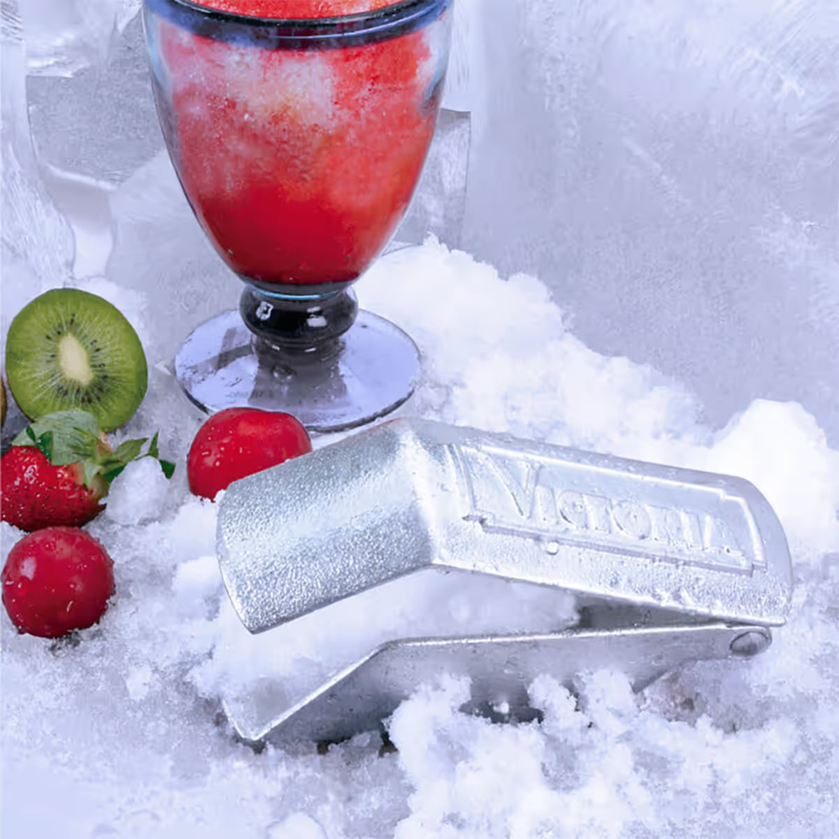 Vista en perspectiva del raspador de hielo manual Victoria en hierro fundido estañado ambientado con hielo raspado, una granizada y frutas frescas - Ferretería La Palma - 1050031