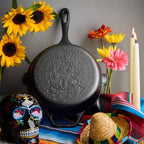 Vista frontal de la base del sartén de hierro fundido Victoria de 25 cm con diseño grabado de Catrina edición especial ambientado con girasoles, velas y elementos decorativos de día de muertos - Almacén La Palma - 1050097