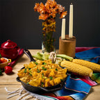 Vista del sartén de hierro fundido Victoria de 25 cm ambientado con nachos, mazorcas de maíz, velas y flores sobre un mantel colorido - Almacén La Palma - 1050097