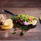 Sartén para fajitas Victoria curado de 24 cm con carne asada, guacamole, vegetales y stack de tortillas sobre una mesa de madera rústica - Ferretería La Palma - 1050060