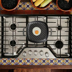 Vista cenital del sartén grill cuadrado Victoria de 25 cm en hierro fundido esmaltado con un huevo frito sobre una estufa de gas en un ambiente de cocina tradicional - Ferretería La Palma - 1050090