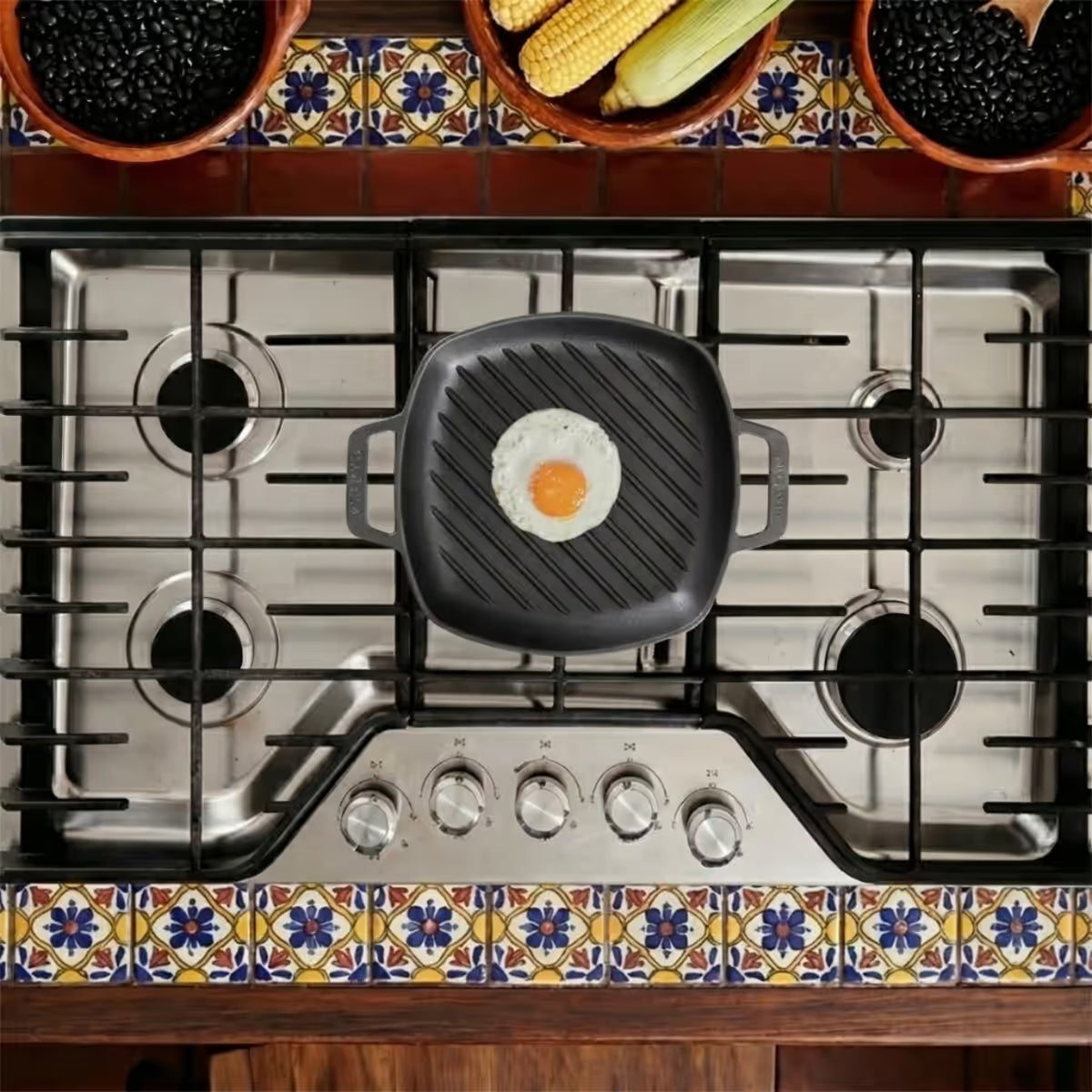 Vista cenital del sartén grill cuadrado Victoria de 25 cm en hierro fundido esmaltado con un huevo frito sobre una estufa de gas en un ambiente de cocina tradicional - Ferretería La Palma - 1050090