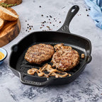 Sartén grill esmaltado Victoria de 25 cm en hierro fundido curado con carnes de hamburguesa y cebollas caramelizadas resaltando las marcas de asado - Ferretería La Palma - 1050027