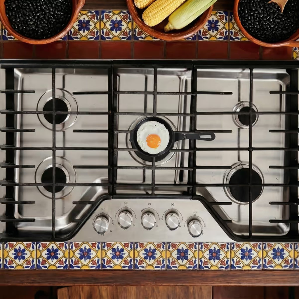 Mini sartén de hierro fundido esmaltado Victoria de 12 cm sobre estufa de gas cocinando un huevo frito en una cocina con azulejos tradicionales - Ferretería La Palma - 1050078