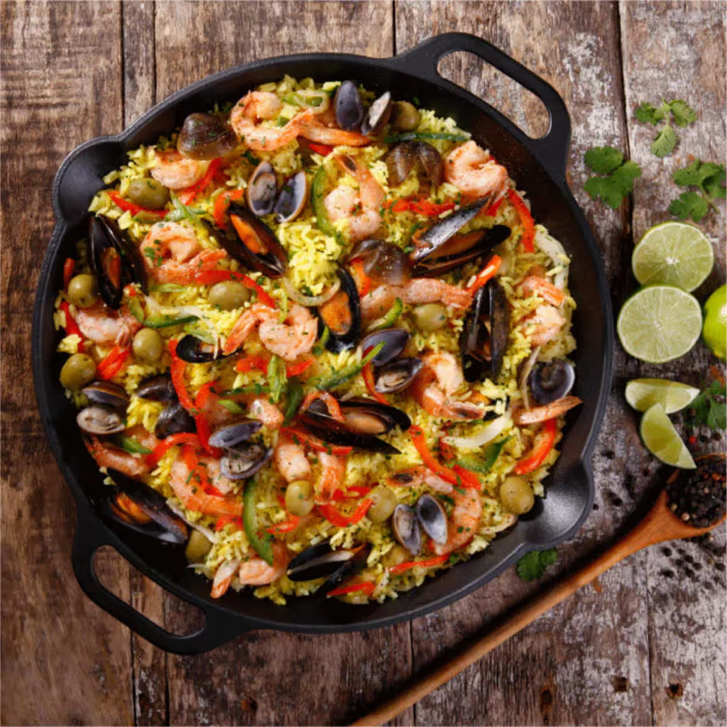 Sartén paellera redonda Victoria de 33 cm en hierro fundido curado con una paella de mariscos recién preparada sobre una superficie de madera rústica - Ferretería La Palma - 1050028
